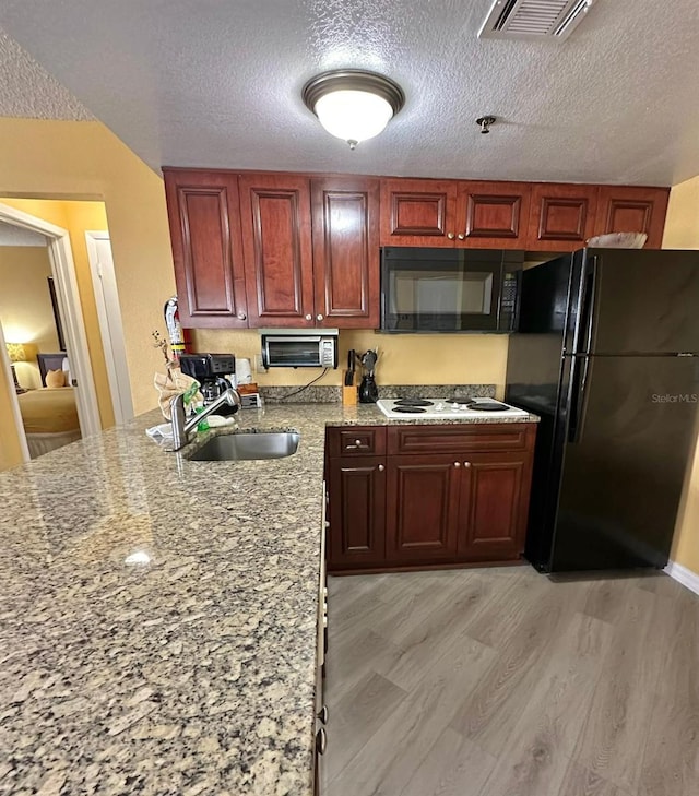 kitchen featuring visible vents, light wood-style flooring, a textured ceiling, black appliances, and a sink