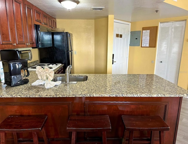 kitchen featuring freestanding refrigerator, electric panel, visible vents, and light stone countertops