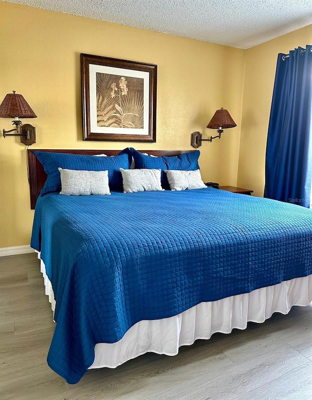 bedroom with a textured ceiling, wood finished floors, and baseboards