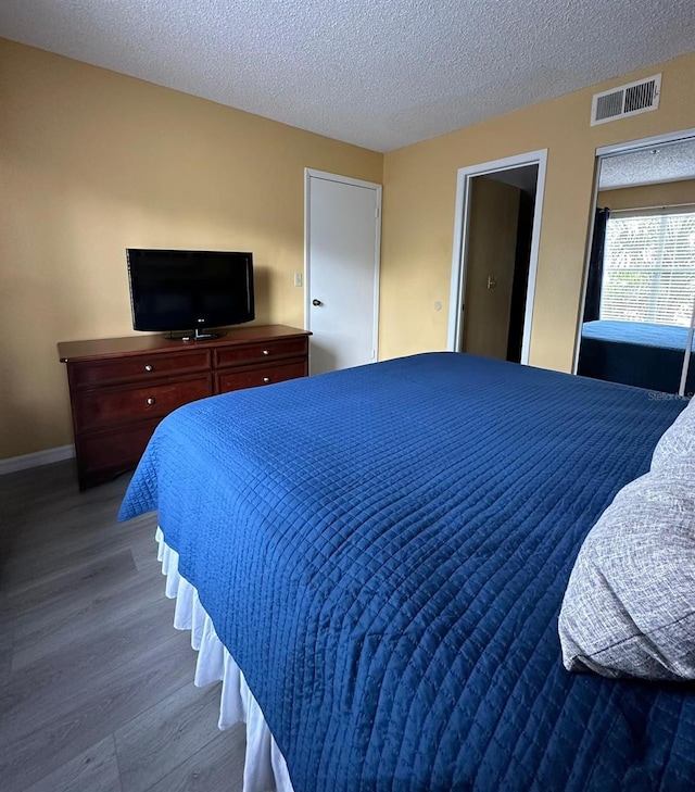 bedroom featuring visible vents, a textured ceiling, baseboards, and wood finished floors