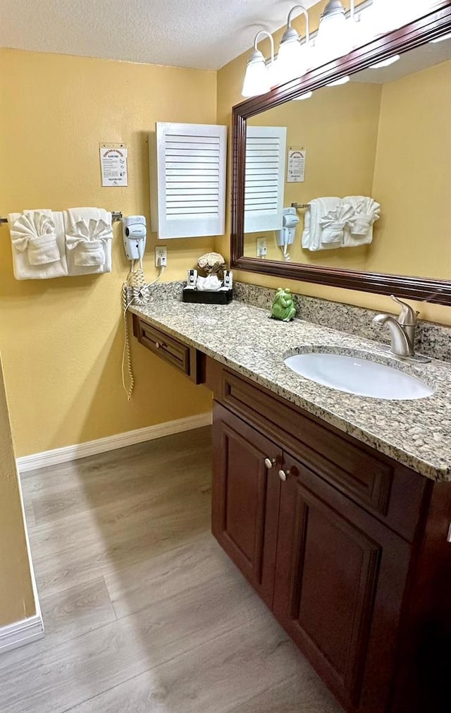 bathroom featuring a textured ceiling, wood finished floors, vanity, and baseboards