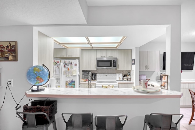 kitchen featuring backsplash, light tile patterned floors, white appliances, and kitchen peninsula