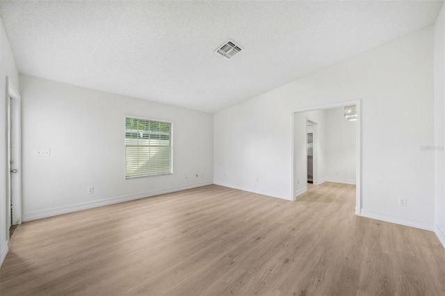 spare room with a textured ceiling, light hardwood / wood-style flooring, and vaulted ceiling