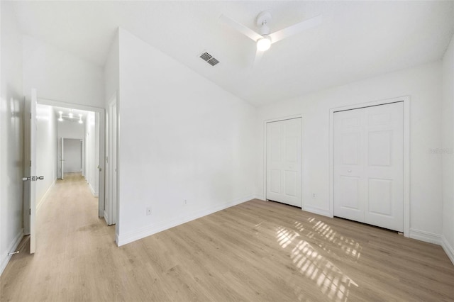 unfurnished bedroom featuring ceiling fan, light hardwood / wood-style floors, vaulted ceiling, and multiple closets