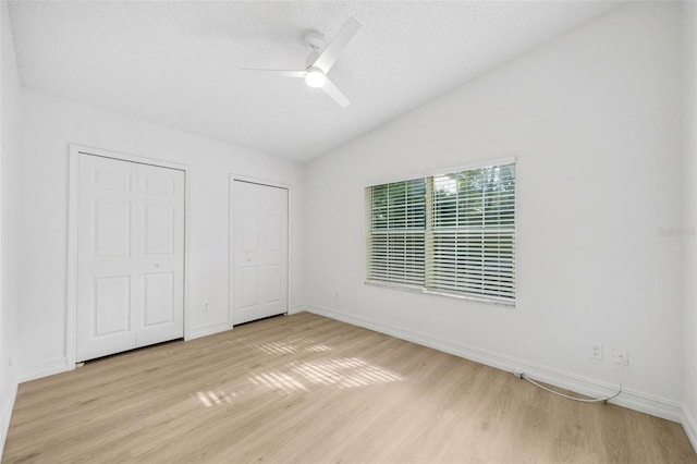 unfurnished bedroom featuring ceiling fan, light hardwood / wood-style floors, and two closets