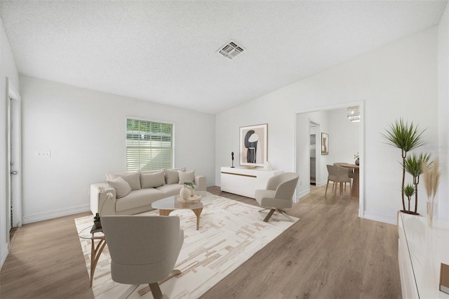 living room with lofted ceiling, a textured ceiling, and light hardwood / wood-style flooring