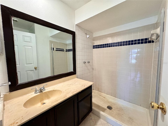 bathroom with tile patterned floors, a tile shower, and vanity