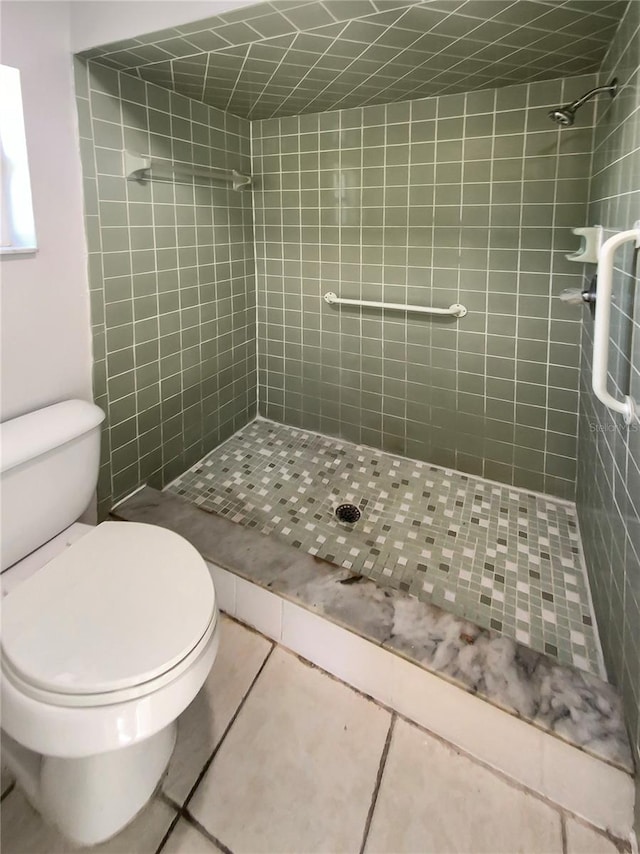 bathroom featuring tile patterned flooring, toilet, and a tile shower