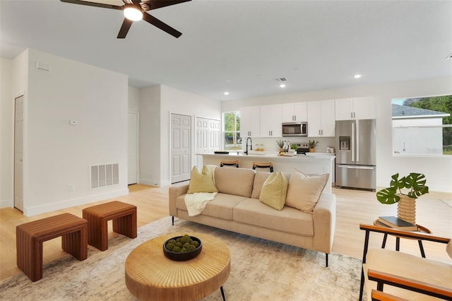 living room featuring light wood-type flooring, ceiling fan, and sink