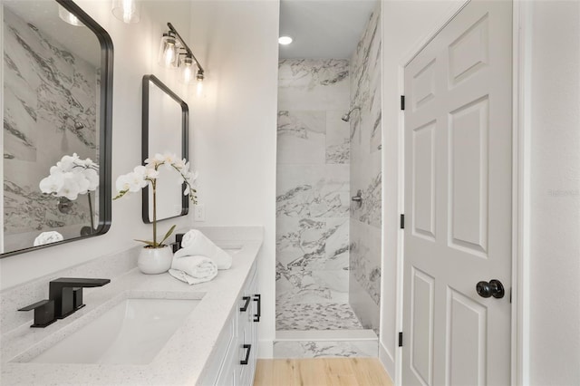 bathroom with hardwood / wood-style flooring, vanity, and tiled shower