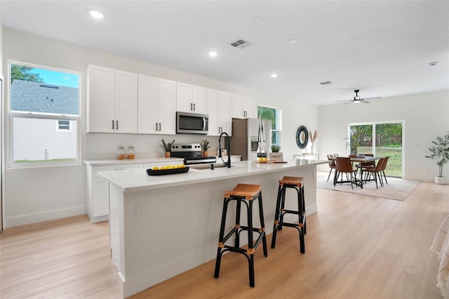 kitchen featuring stainless steel appliances, a center island with sink, light hardwood / wood-style flooring, and white cabinets