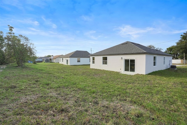 rear view of house featuring central AC unit and a lawn