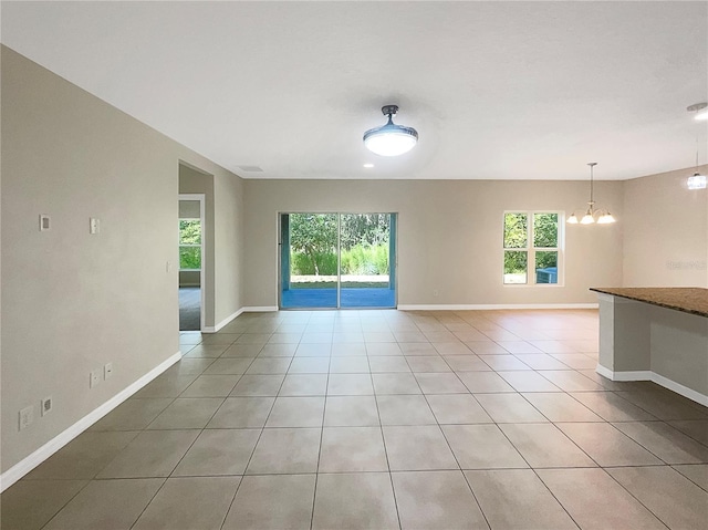 empty room with an inviting chandelier, baseboards, and light tile patterned floors