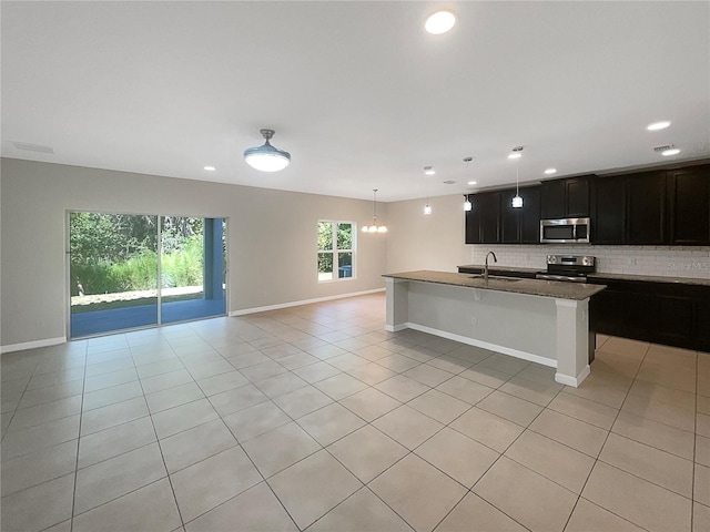 kitchen featuring light tile patterned floors, open floor plan, a sink, stainless steel appliances, and backsplash