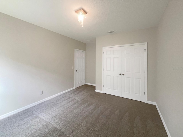 unfurnished bedroom with dark colored carpet, a closet, visible vents, and baseboards