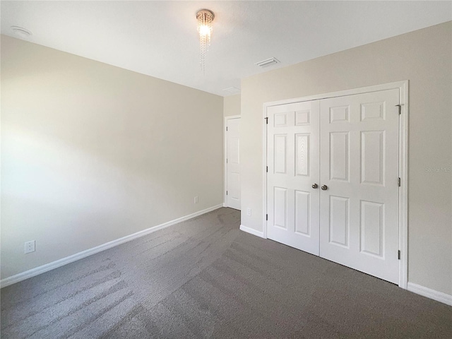 unfurnished bedroom with a closet, visible vents, dark carpet, and baseboards