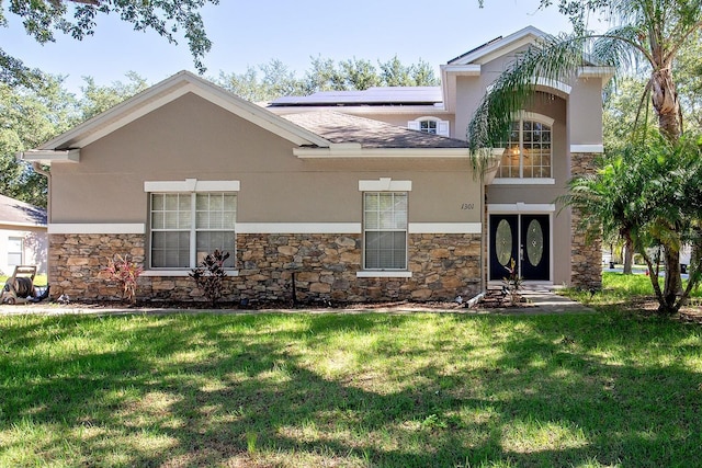 view of front of home with stone siding, stucco siding, a front yard, and roof mounted solar panels
