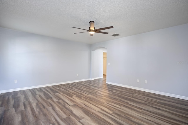 unfurnished room with visible vents, baseboards, ceiling fan, dark wood finished floors, and arched walkways