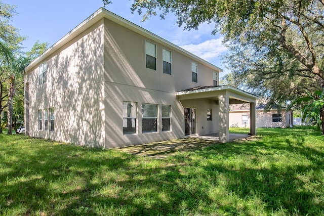 rear view of house with stucco siding, a patio, and a yard