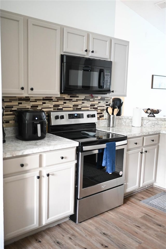 kitchen with light stone counters, stainless steel electric stove, tasteful backsplash, and light hardwood / wood-style flooring