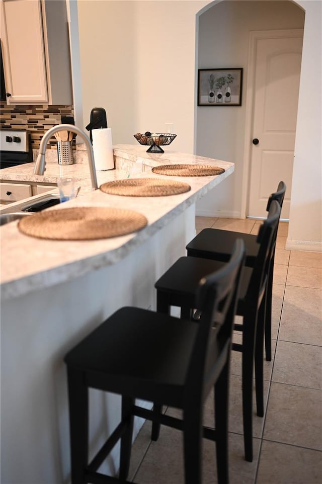 kitchen featuring tasteful backsplash, light stone counters, light tile patterned floors, and white cabinets