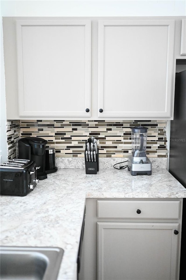 kitchen featuring white cabinetry, decorative backsplash, and black fridge