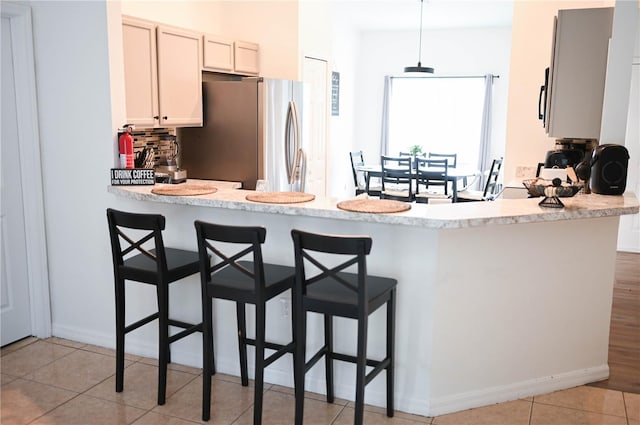 kitchen with light tile patterned floors, stainless steel fridge, kitchen peninsula, a breakfast bar area, and tasteful backsplash