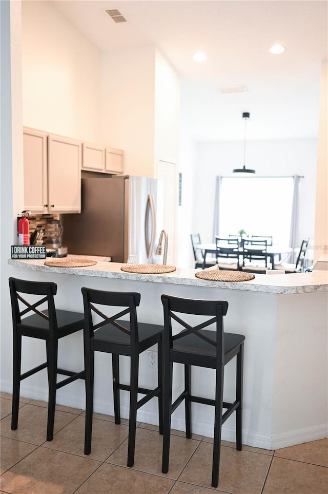 kitchen with hanging light fixtures, stainless steel refrigerator, kitchen peninsula, light tile patterned flooring, and a breakfast bar