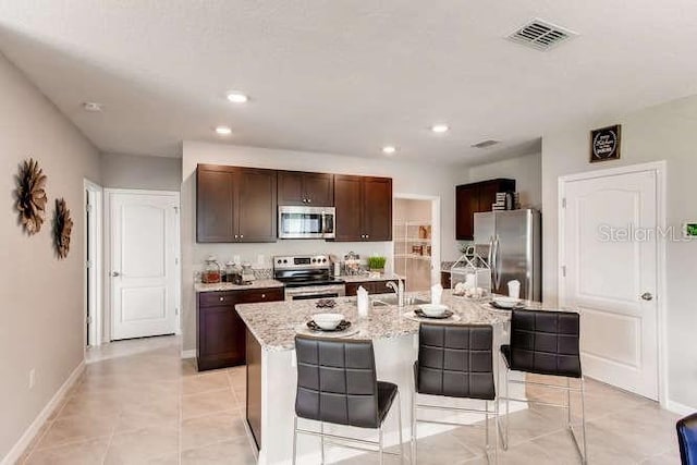 kitchen featuring appliances with stainless steel finishes, a kitchen bar, light stone countertops, and a kitchen island with sink