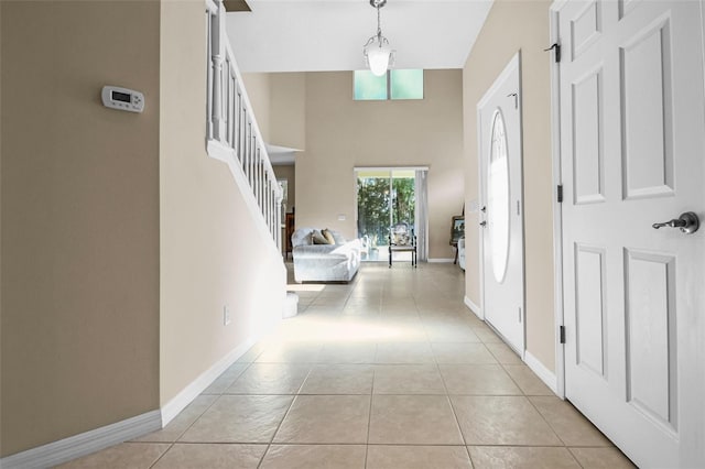 hall featuring a high ceiling, stairway, baseboards, and light tile patterned floors