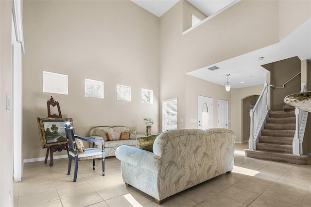 living area featuring visible vents, baseboards, a towering ceiling, stairway, and light tile patterned flooring