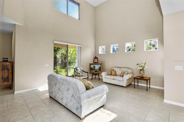 living area with a towering ceiling, light tile patterned floors, and baseboards