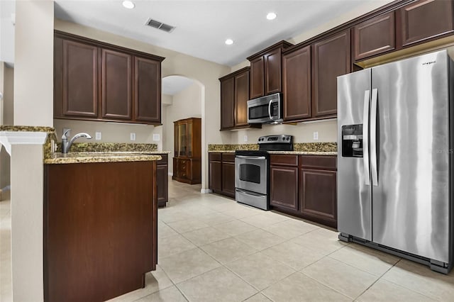 kitchen with arched walkways, light tile patterned flooring, visible vents, appliances with stainless steel finishes, and light stone countertops