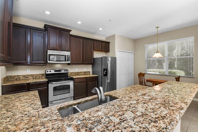 kitchen featuring appliances with stainless steel finishes, a sink, light stone counters, and dark brown cabinets