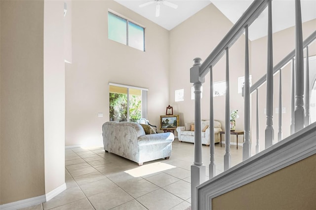 living room with light tile patterned flooring, a high ceiling, a ceiling fan, baseboards, and stairway