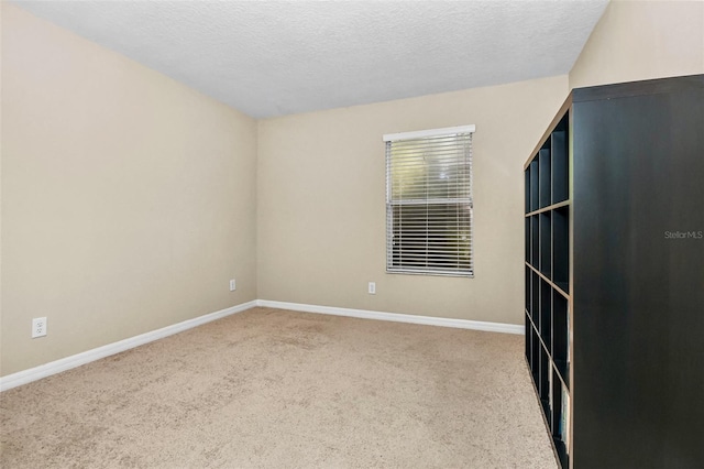 spare room with a textured ceiling, carpet, and baseboards