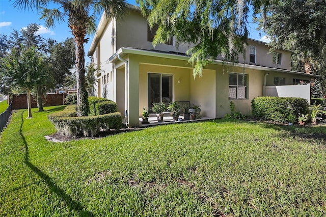 rear view of house featuring fence, a lawn, and stucco siding