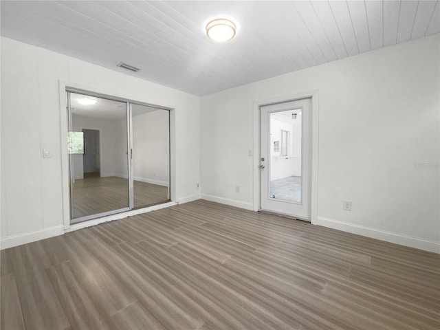 empty room featuring wood finished floors, visible vents, and baseboards