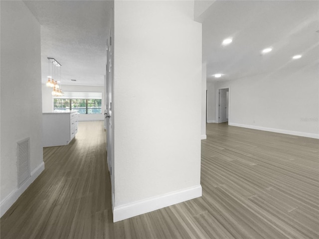 corridor with a chandelier, recessed lighting, wood finished floors, visible vents, and baseboards