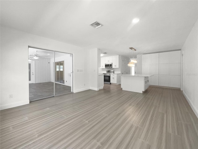 unfurnished living room with ceiling fan with notable chandelier, light wood-style flooring, visible vents, and baseboards