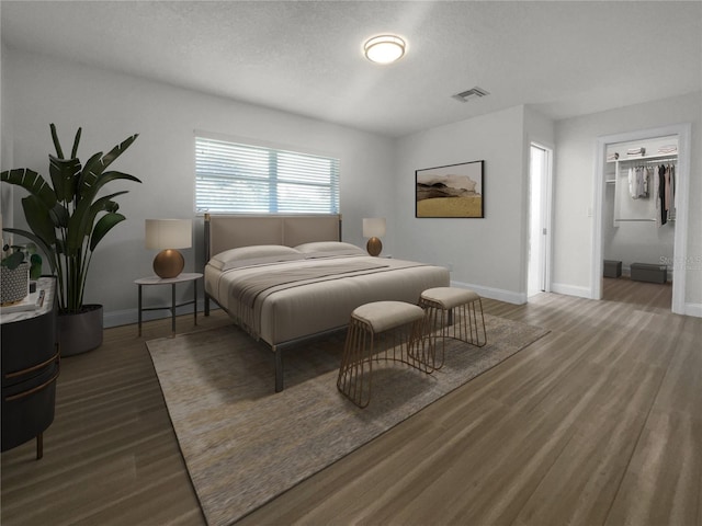 bedroom with visible vents, a textured ceiling, baseboards, and wood finished floors