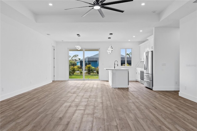 unfurnished living room with plenty of natural light, sink, light wood-type flooring, and a tray ceiling