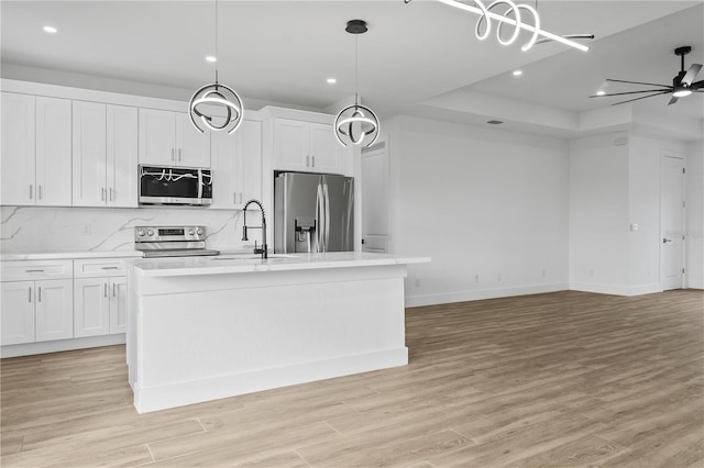 kitchen featuring sink, white cabinetry, pendant lighting, stainless steel appliances, and a kitchen island with sink