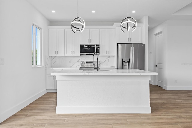 kitchen featuring stainless steel appliances, an island with sink, pendant lighting, and white cabinets