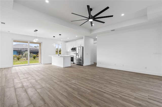 unfurnished living room featuring ceiling fan with notable chandelier, light hardwood / wood-style floors, and a raised ceiling