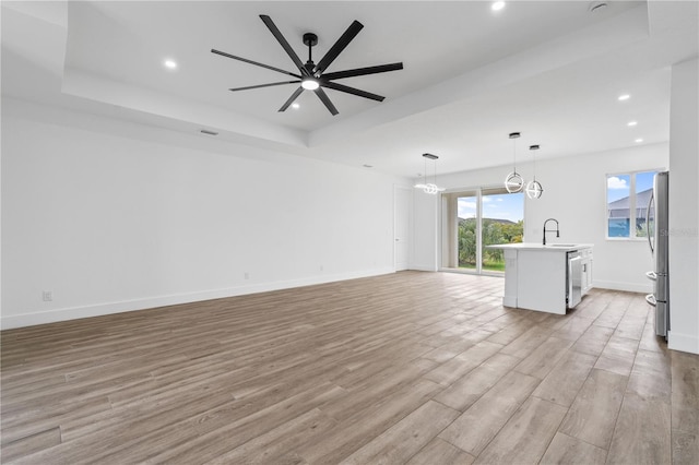 unfurnished living room with sink, a tray ceiling, light hardwood / wood-style floors, and ceiling fan