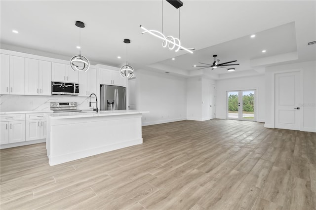 kitchen featuring appliances with stainless steel finishes, a tray ceiling, an island with sink, pendant lighting, and white cabinets