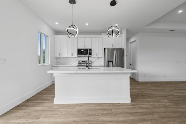 kitchen featuring white cabinetry, stainless steel appliances, tasteful backsplash, a center island with sink, and decorative light fixtures