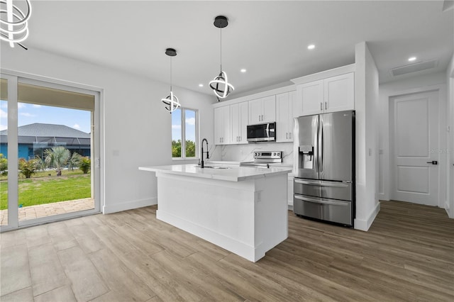 kitchen with sink, decorative light fixtures, a center island with sink, stainless steel appliances, and white cabinets