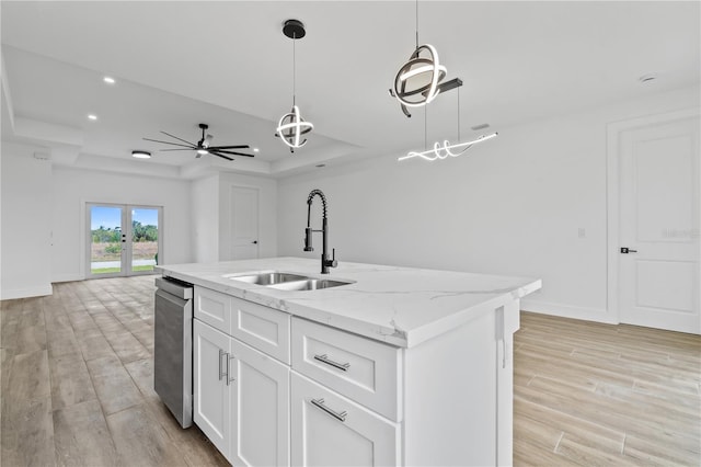 kitchen with sink, white cabinetry, hanging light fixtures, a tray ceiling, and light stone countertops